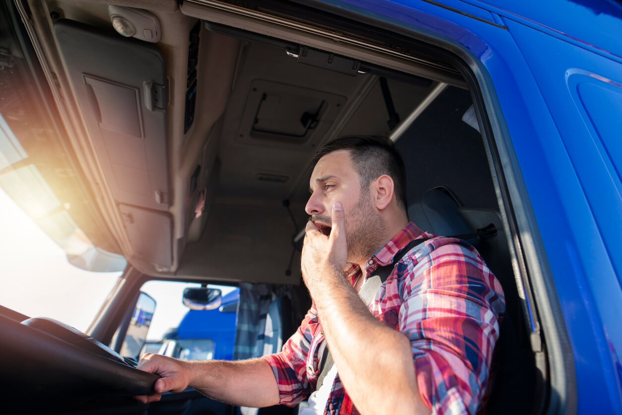 Fatigued Driver Truck Accidents driver in blue truck yawning while driving with hand over his mouth