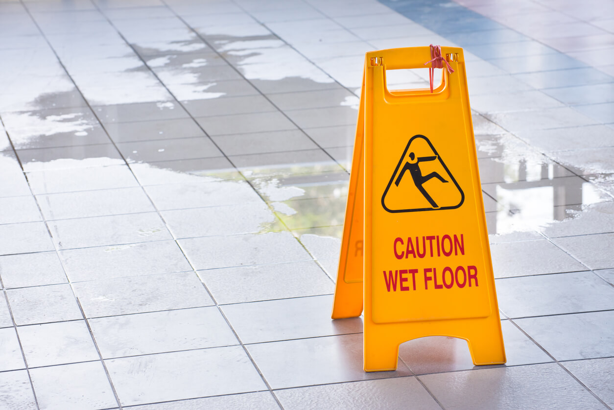Slip and Fall Accident yellow caution wet floor sign in front of large puddle of water