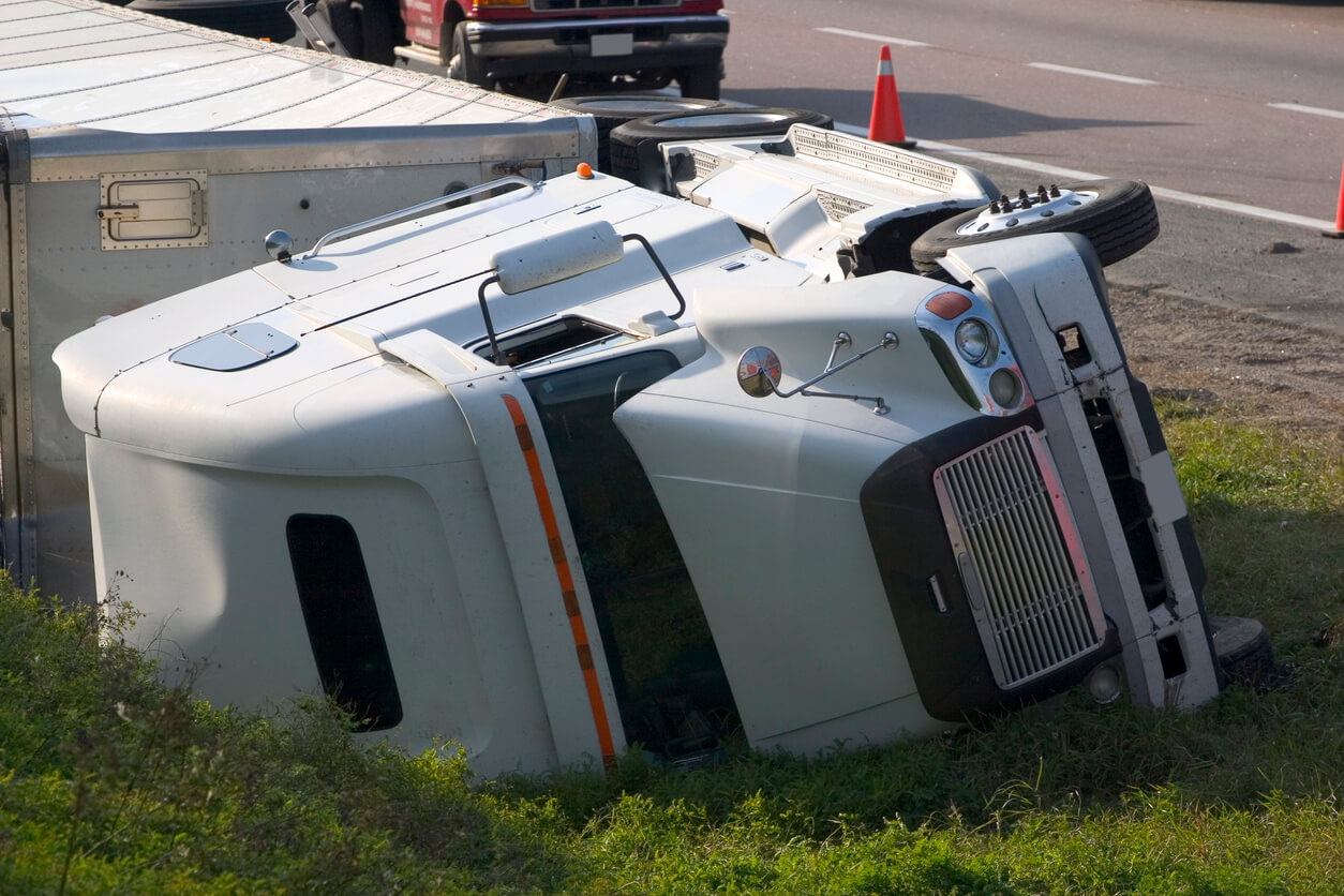 Truck Accidents large white truck fallen on its side on grassy area on side of the road